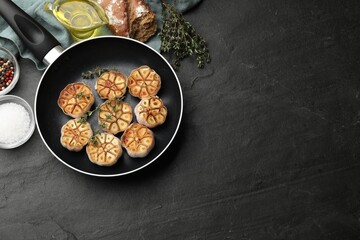 Grilled garlic with spices and bread on black table, flat lay. Space for text