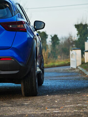Fototapeta premium A blue car is parked in front of a white house. The car is parked on a wet road, and the reflection of the car can be seen in the water. The scene is calm and peaceful. Rural country side area.