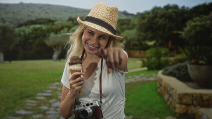 Woman holding ice cream cone and vintage camera, points finger toward viewer in forest path;...