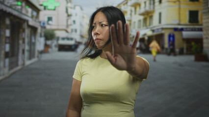 Fototapeta premium Young woman holds palm out toward camera on city street to block approach and set boundary; defiance boundary protection.