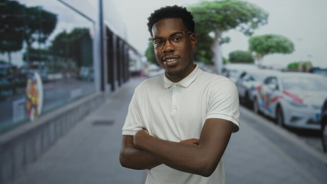 Young african american man wearing glasses with crossed arms and bare arms on city street; defiance.