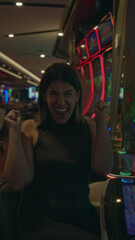 Fototapeta premium Woman presses a slot machine button with hand on button, smiling while seated by neon slot machines in casino; joyful anticipation.
