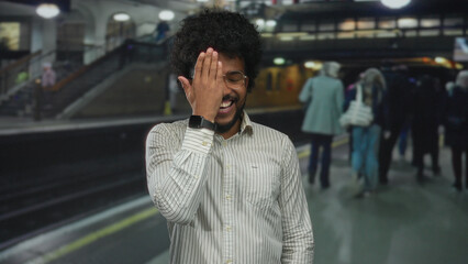 Fototapeta premium African american man smiling at train station platform with blurred train and crowd in background, conveying urban travel setting.