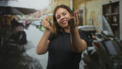 Fototapeta premium Woman making finger heart with fingers and hands while standing on a street terrace at a restaurant; playful affection.