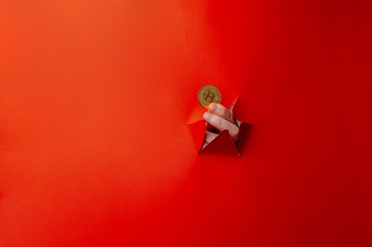 Gold Coin Through Torn Red Paper Held By Hand Representing Bitcoin And Crypto Investment, Blockchain Finance,