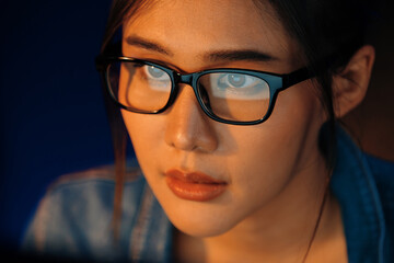 Fototapeta premium Portrait young beautiful Asian creative with glasses of serious face looking on pc to search project creator social media online, planning strategy creator at neon modern office at night. Stratagem.
