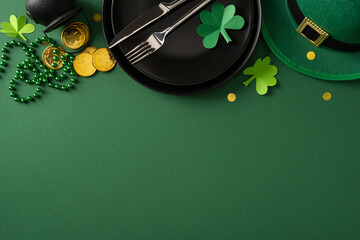 Fototapeta premium Festive St Patrick's Day table scene with shamrock decorations, gold coins, green beads and a leprechaun hat arranged around a black plate and cutlery