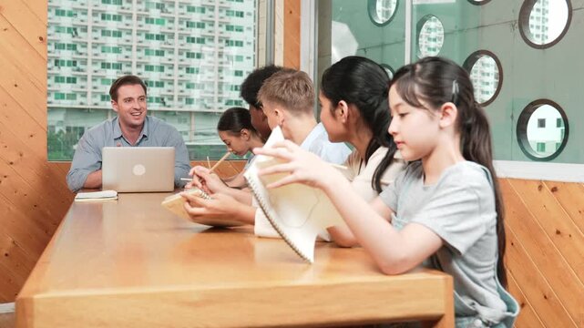 Asian girl laughing at caucasian boy idea while professional teacher teaching about program. Happy diverse student work classwork while sitting at classroom. Creative education concept. Edification