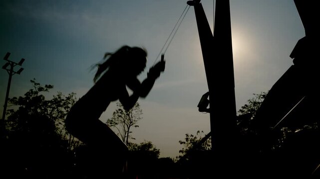 Silhouette female athlete training on outdoor fitness machine at sunset. Strength, endurance and active lifestyle concept. Dramatic backlight sport workout with copy space.