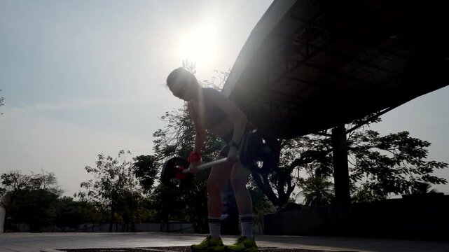 Athletic woman performing barbell bent over row exercise in outdoor park. Functional strength and endurance training concept with natural sunset light.