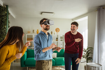 Obraz premium Friends laughing watching man using virtual reality headset