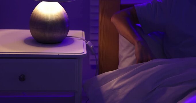 Man turning on night lamp and adjusting pillow in bed