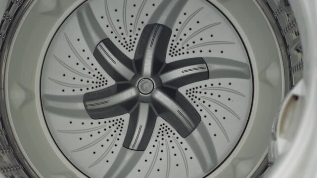Close up slow motion top-down view inside washing machine, silver drum and agitator rotating to wash clothes
