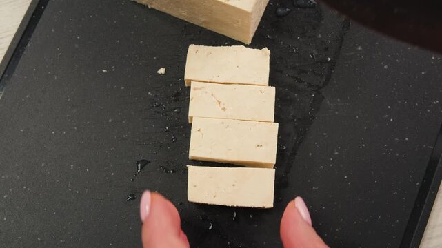 Chef cut cheese for Fried tofu with sesame seeds and spices on cast iron pan, cooking japanese salad. Healthy ingredient for cooking vegan vegetarian diet food. Roasted tofu over black background.