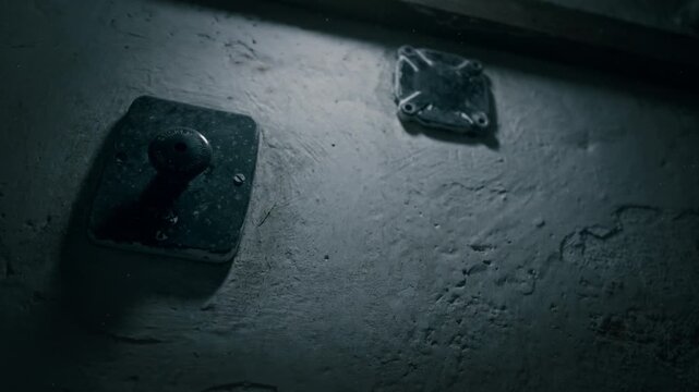Electrical panel attached to rough plaster in blue tinted darkness. Gritty utility detail ideal for sabotage, danger, or investigation themes.