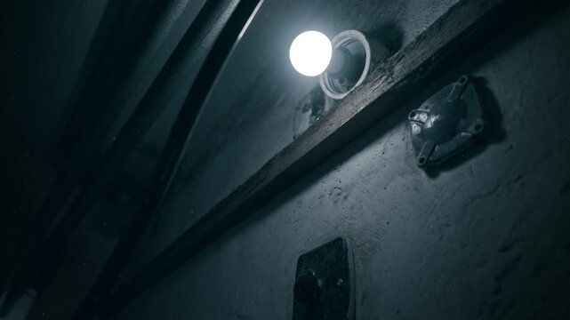 Bare light source flashes against rough interior in cold blue tone. Stark atmosphere ideal for interrogation, captivity, or crime settings.