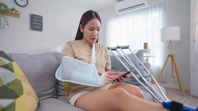Injured Asian young woman chatting on phone in cozy living room at home. 