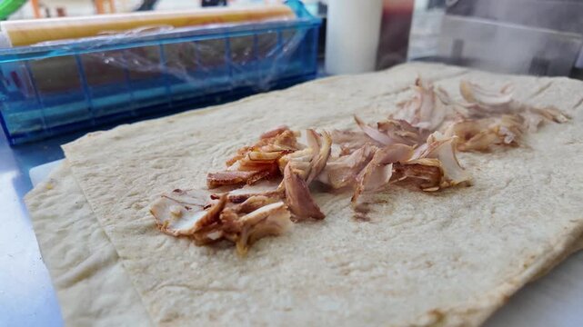 Chef placing hot grilled chicken slices on flatbread to prepare shawarma wrap with steam rising in slow motion