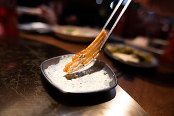 Close-up of chopsticks lifting spicy fried food from creamy sauce in dark bowl on wooden table © chuangxin
