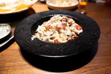 Creamy pasta with tomatoes and herbs served in black bowl on wooden table