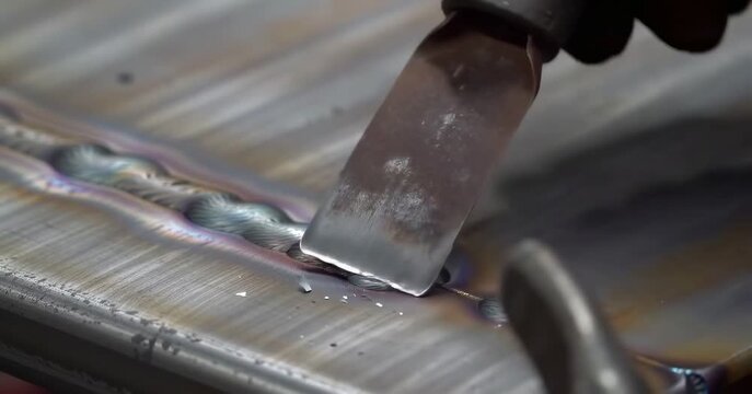Chisel scraping molten metal on shiny steel surface
