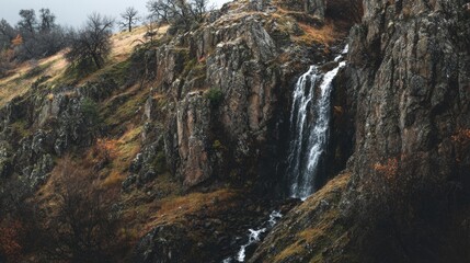 Obraz premium Cascading Waterfall Down a Rugged Rocky Cliffside in a Natural Landscape
