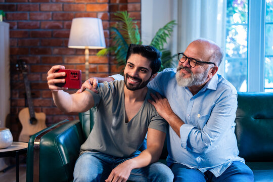 Indian retired Smiling dad and adult son capturing selfie a cheerful indoor memory.