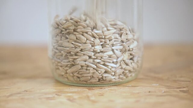 Shelled sunflower seeds falling and filling a glass jar