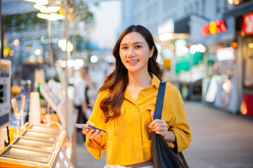 An Asian woman is strolling through a night market, enjoying traditional street food, colorful lanterns, and smiling at the bustling city stalls. It's a vibrant atmosphere and a wonderful cultural 