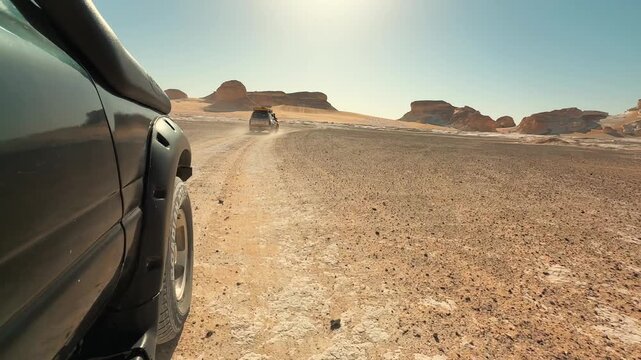 Side POV from moving cars follow each other on off road in the desert