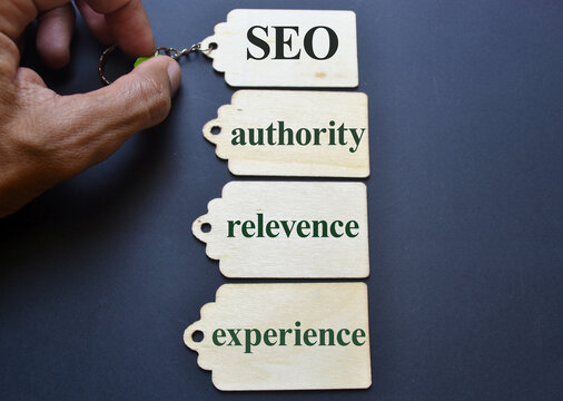 Hand holding keychain with wooden tags labeled seo authority relevance and experience on dark background symbolizing digital marketing strategy, search optimization, and online visibility for editoria