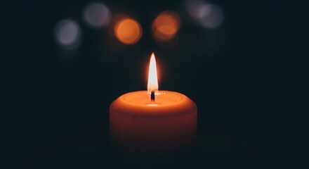 Close-up of a lit candle with warm orange flame and soft bokeh background