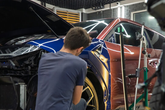 Process of paintless dent repair on car body. The mechanic at the auto shop with tools to repair dents in car body. Body repair. PDR. A specialist repairs a dent on the car body without painting.