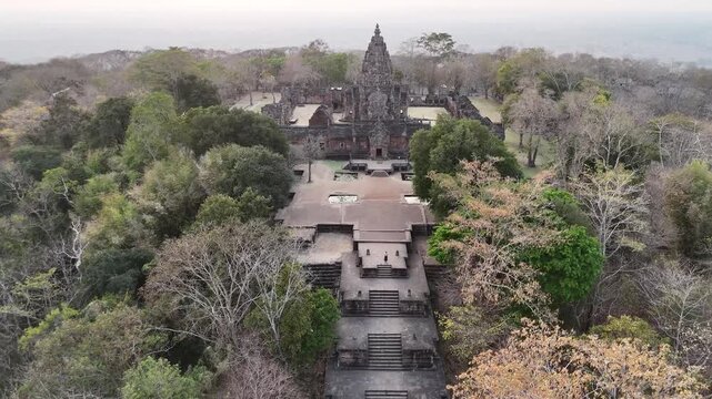 Aerial fly-through towards Prasat Phnom Rung main tower at sunset, drone entering ancient temple complex.