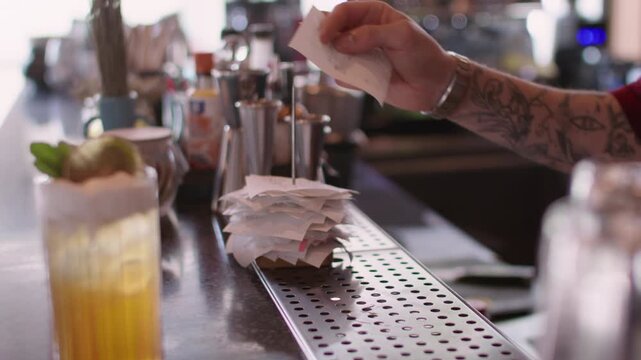 Cafeteria management. Bartender workflow. Worker hand pinning paper receipt to pile on metal spike holder counter. Busy cocktail bar shift result.