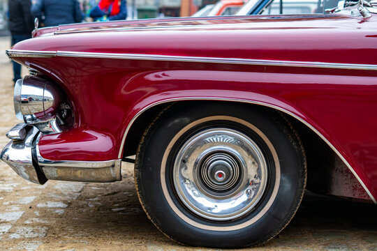 Classic maroon vintage car with chrome bumpers and whitewall tires, close-up of the front fender and stylish hubcap during an antique automobile show in the city.