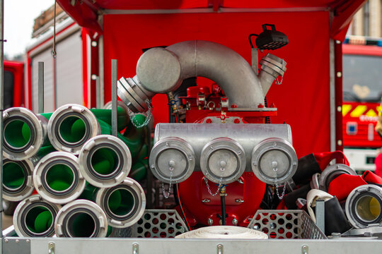 Firefighting power pump with suction and delivery hoses inside a fire truck compartment, professional volunteer fire department rescue equipment for water supply during firefighting operations.