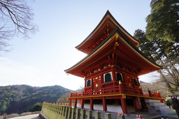 Obraz premium Stunning vibrant red two-story Japanese Buddhist pagoda at Katsuo-ji Temple in Osaka. Traditional temple architecture set against a lush mountain forest backdrop under a clear blue sky. Symbol of peac