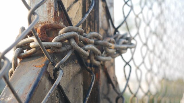 Heavy weathered metal chain wrapped around rusty steel fence post securing chain link fencing in industrial outdoor setting