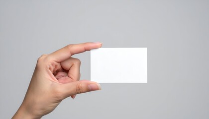 Obraz premium A hand holding a blank white card against a neutral gray background, emphasizing minimalism