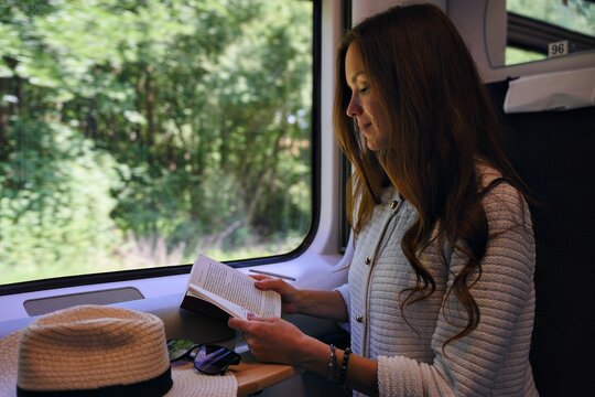 Woman reading by train window as green countryside passes outside