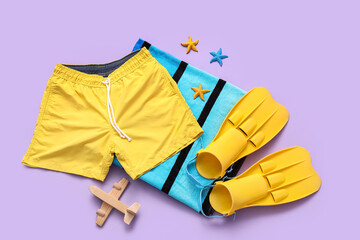 Swimming trunks with airplane and beach accessories on lilac background © Pixel-Shot