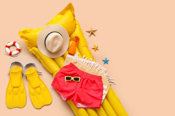 Swimming trunks with inflatable mattress and beach accessories on beige background © Pixel-Shot