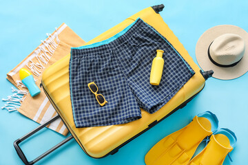 Suitcase with swimming trunks and beach accessories on blue background © Pixel-Shot