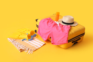 Suitcase with swimming trunks and beach accessories on yellow background © Pixel-Shot