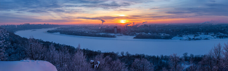 Fototapeta premium Nizhny Novgorod lower city view along Oka river at sunset in winter. The area before cable car construction from Zarechnaya to Switzerland Park. Panorama in golden hour light over the urban landscape
