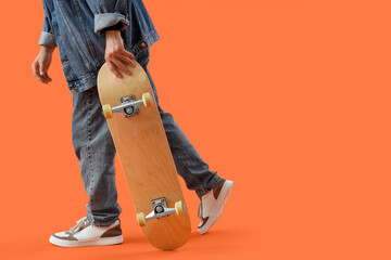 Legs of young man with skateboard on orange background, closeup © Pixel-Shot