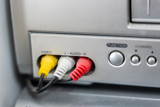 Close up of RCA composite output on VCR front panel. Yellow video and red white audio connectors plugged into analog AV output ports. Retro home electronics detail.