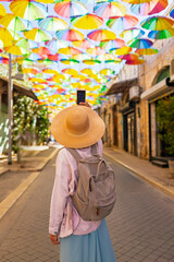 Fototapeta premium Girl Tourist on an excursion stands on the street with hanging umbrellas and takes pictures. umbrella sky.