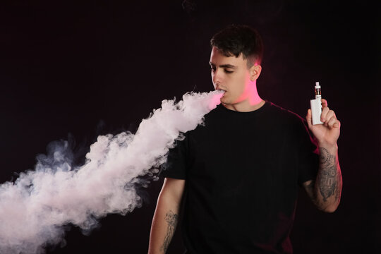 Handsome young man smoking electronic cigarette on dark background